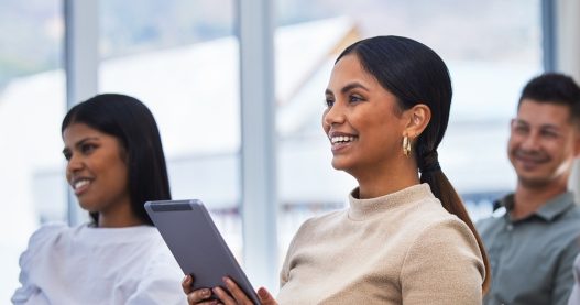 Shot of a young woman using a tablet  and laughing during a meeting at work.
